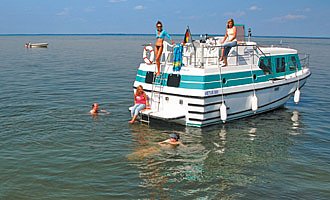 unser Hausboot vetus 900 ist auf der Müritz vor Anker und Leute baden im See.