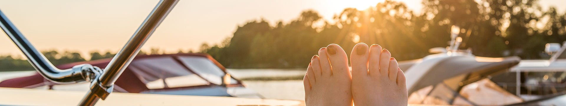 Eine Frau sitzt an der Spitze eines Bootes, die Arme erholsam weit ausgestreckt und schaut dabei in die Ferne über den See.