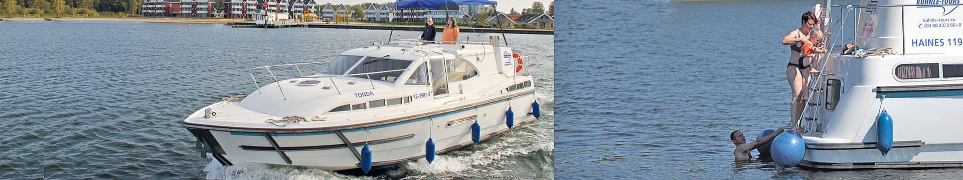 Zwei Boote der Marke Haines begegnen sich auf einem See, an dessen Ufer weitere Boote zu sehen sind. Die Besatzung sitz locker verteilt außen an Bord.